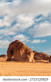A dramatic desert landscape featuring a massive sandstone arch amid red sand and open plains, under a bright blue sky with fluffy clouds. Evokes adventure, exploration, and ancient geology.