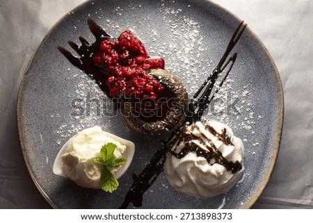 dramatic dessert closeup of lava cake with raspberry compote and whipped cream, chocolate drizzle and powdered sugar, latenight