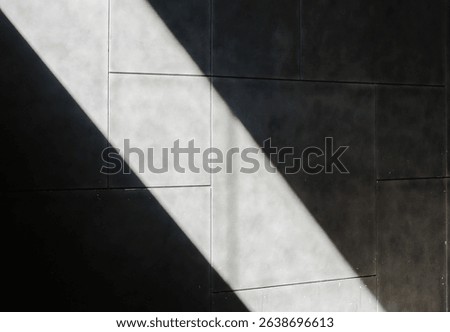 A dramatic diagonal shaft of bright sunlight cuts across a textured dark grey wall, creating a striking contrast of light and shadow. Ideal for abstract backgrounds.