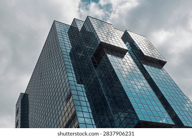 Dramatic diagonal view of a postmodern glass office tower with cantilevered volumes in the City of London against a stormy sky.
