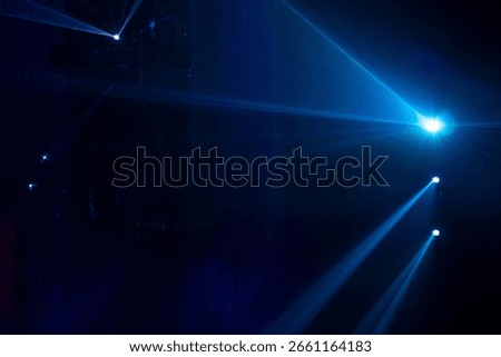 A dramatic display of laser or stage lighting in a dark atmosphere, typically seen at concerts, clubs, or immersive light shows. Blue and purple beams in dark background.