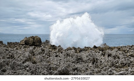 A dramatic display of ocean power as a massive wave crashes against the sharp, volcanic rock formations. The contrast between the rough, jagged stone and the explosive white sea spray creates a breathtaking moment captured in time.
