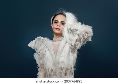 Dramatic Drag Queen, Young Transgender With Rubbed Bright Night Makeup Wearing Boa Feather Party Dress Taking Off White Wig, Posing Isolated Over Blue Background. Lgbtqi, Drag Show Concept