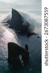 Dramatic Drangarnir cliffs tower above the serene waters of the Faroe Islands, shrouded in mist. This stunning natural formation captivates with its rugged beauty and tranquil atmosphere at twilight.