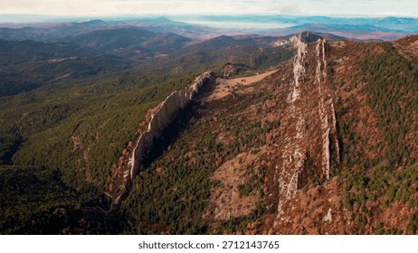 Dramatic drone perspective flying along the immense vertical cliffs of the Rallas de Santo Domingo, revealing the intricate textures and geological fault line surrounded by a dense autumn forest.