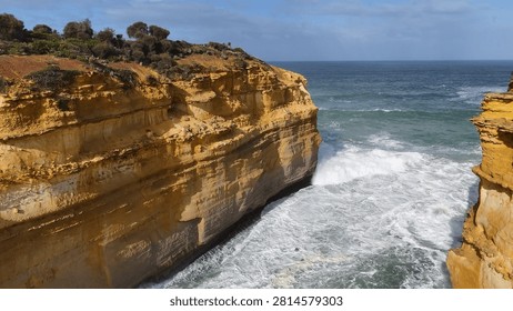 Dramatic drone shot of rugged limestone cliffs meeting churning ocean waves in Victoria, Australia.