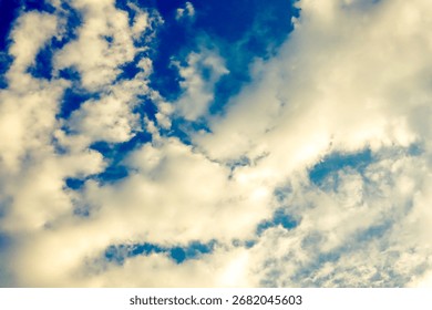A dramatic and dynamic sky is filled with a mixture of bright, fluffy clouds and deep blue patches. The clouds appear to be illuminated from above, with a warm.