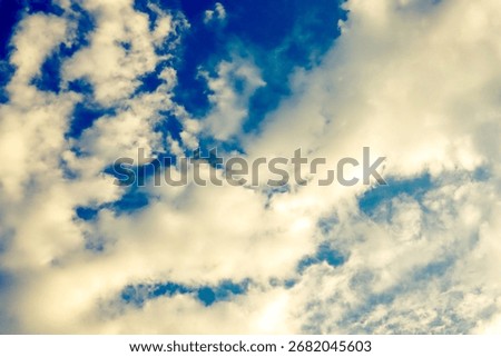 A dramatic and dynamic sky is filled with a mixture of bright, fluffy clouds and deep blue patches. The clouds appear to be illuminated from above, with a warm.