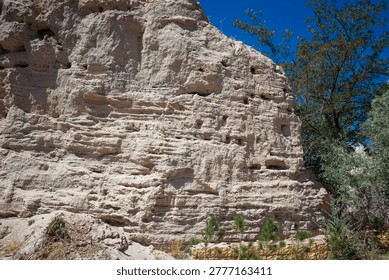 Dramatic eroded tuff rockface in Cappadocia's fairy chimneys near Ürgüp, riddled with ancient cave dwellings and troglodyte openings. Layered volcanic formations evoke Ancient Anatolia's Seljuk architecture at Osiana, Hagios Prokopios, Başköy. Arid bushes, pines frame blue sky vista. Perfect for tourism ads, geology docs, travel mag covers boosting wanderlust escapes.