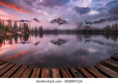 Dramatic evening near mountain lake Štrbské pleso with colorful clouds and water reflection. Wooden pier in High Tatras NP, Slovakia