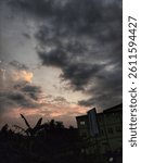 Dramatic evening sky with dark clouds and glowing sunset light over silhouettes of trees and buildings in a tropical urban area.
