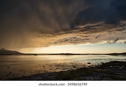 Dramatic evening storm clouds at stunning evening over the beach at Mjelle in Northern Norway pouring rain over the bay