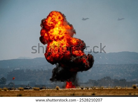 A dramatic explosion of military munitions with a ball of orange fire and jets flying in the background