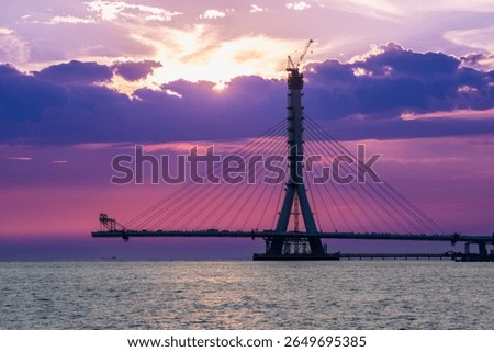 A dramatic and fiery sunset casts a vivid glow over the silhouette of the Danjiang Bridge under construction in Tamsui District New Taipei City Taiwan, enhancing the twilight scene.
