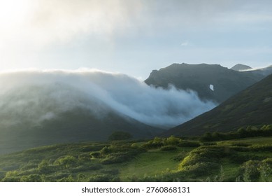 Dramatic fog and low clouds moving through lush green mountains in the wild nature of Kamchatka, Russia. Scenic remote wilderness landscape with untouched alpine terrain.
