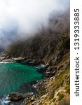 Dramatic fog settles over cliffs and turquoise water of Hout Bay on Chapman
