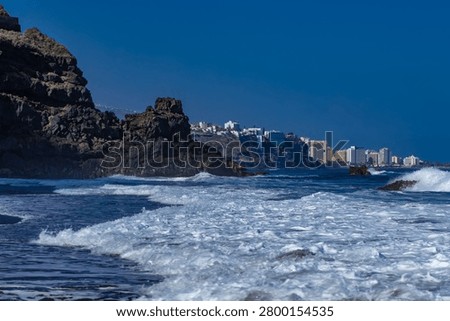 Dramatic footage of powerful Atlantic Ocean waves crashing against the rocky coastline of Tenerife, Canary Islands. Rough sea conditions, dangerous surf, and strong currents make swimming unsafe near the black volcanic sand beach. Natural forces, coastal hazards, extreme weather, and the rugged beauty of the volcanic shoreline create a striking travel and nature scen
