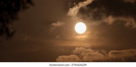 Dramatic full moon or bright sun shining through dark, moody clouds in a sepia-toned sky