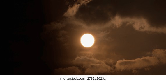 Dramatic full moon or bright sun shining through dark, moody clouds in a sepia-toned sky