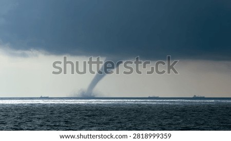 A dramatic funnel cloud descends from a massive, dark storm system, touching down on the surface of a vast body of water.