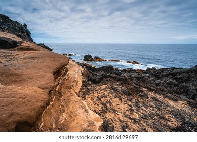 Dramatic geological formations of dark lava rock and red sandstone border the deep blue Atlantic waters near Buenavista del Norte