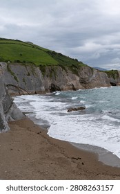 Dramatic geological formations meet the ocean waves on a sandy beach in Zarautz, Basque Country