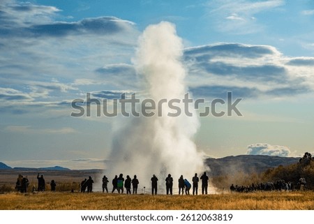 A dramatic geyser Strokkur eruption captured with a crowd of onlookers enjoying the impressive natural display. Golden Circle attraction.