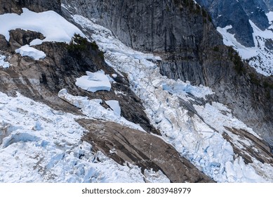 Dramatic glacial icefall cascading over steep rocky cliffs with crevasses and snow in British Columbia, Canada.
