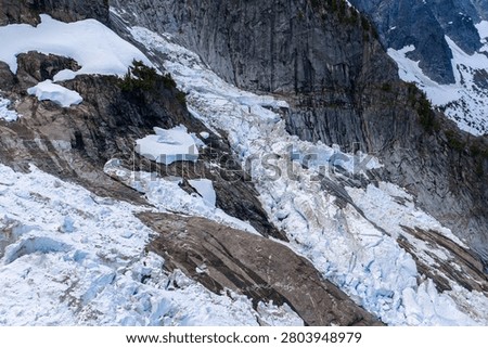 Dramatic glacial icefall cascading over steep rocky cliffs with crevasses and snow in British Columbia, Canada.