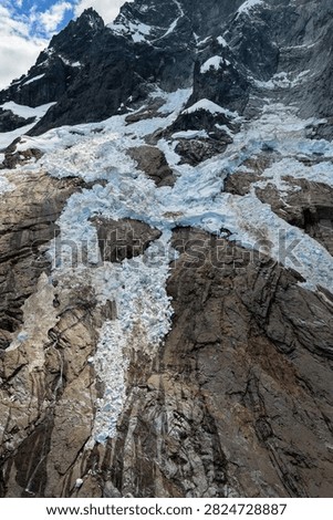 Dramatic glacier icefall cascades over rocky mountain cliffs, showing blue ice, crevasses and alpine terrain in British Columbia, Canada.