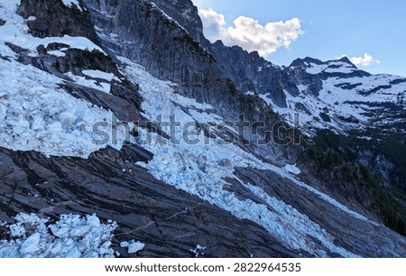 Dramatic glacier icefall descending a rocky alpine slope beneath snow-covered peaks in British Columbia, Canada, evoking cold, remote wilderness and rugged geology.