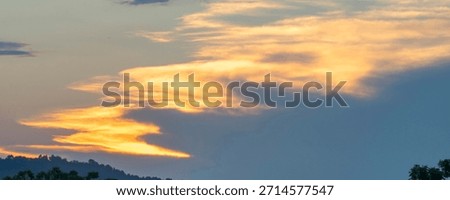 Dramatic golden clouds form a fiery, dragon-like shape against a deep blue sky at sunset. This majestic, abstract skyscape evokes a sense of power and myth. Ideal for fantasy or creative concepts.