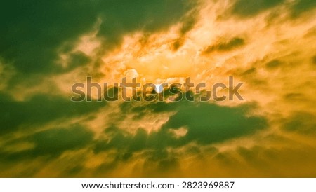 Dramatic Golden Evening Sky and Sun Over Jakarta. Captivating wide-angle photograph capturing the dramatic transition of the evening sky over Jakarta at 16:48. The image features the sun as a bright, distinct orb breaking through a dynamic blanket of heavy, textured clouds. A striking color palette defines the scene, blending rich golden-orange light with deep, moody olive-green and gray cloud formations. Radiating sunbeams pierce downward through the atmospheric haze, creating a powerful sense of depth, scale, and natural majesty. This evocative cloudscape perfectly illustrates tropical weather patterns, atmospheric pollution, climate variations, or a beautiful sunset transition in an urban environment. Ideal for editorial use, weather reporting, environmental concepts, background designs, and commercial creative projects seeking a bold, high-contrast, and emotionally resonant nature backdrop.