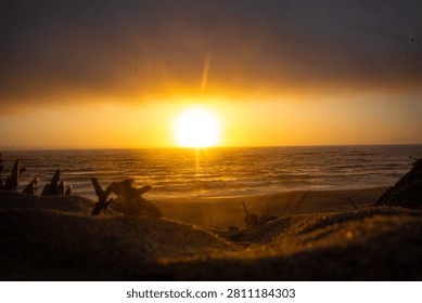 Dramatic golden hour sunset over the Pacific Ocean with a brilliant sunburst breaking under a heavy bank of dark clouds, California coast.