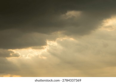 Dramatic golden sun rays breaking through dark stormy clouds creating a spectacular light effect in the sky