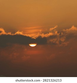 Dramatic Golden Sunset Behind Clouds
Description: A breathtaking view of a brilliant golden sun peeking through a thick horizontal band of dramatic clouds at sunset, filling the sky with a warm amber and orange glow.