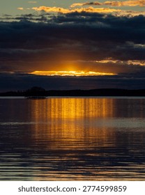 Dramatic Golden Sunset Breaking Through Dark Storm Clouds Over Finnish Lake with Island Silhouette