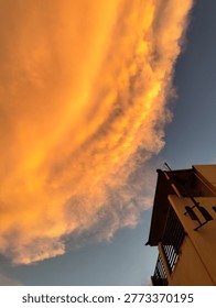 Dramatic golden sunset clouds over residential building with blue sky, urban skyscape and warm evening atmosphere