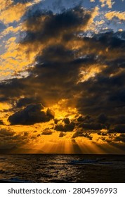 Dramatic golden sunset over the ocean with divine light rays breaking through heavy, textured storm clouds - Stunning seascape featuring sunbeams piercing dark clouds during a vibrant, fiery sunset.