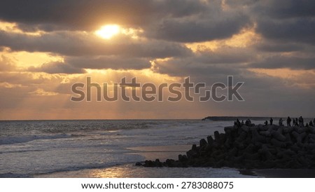 Dramatic golden sunset over the ocean with sun rays breaking through storm clouds and waves crashing on the shore.