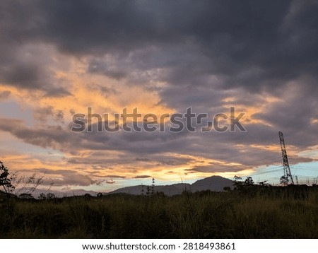 Dramatic golden sunset sky with dark clouds over landscape with electricity pylon tower