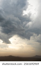 Dramatic gray storm clouds in the sky over mountain landscape during orange sunset in South Africa.