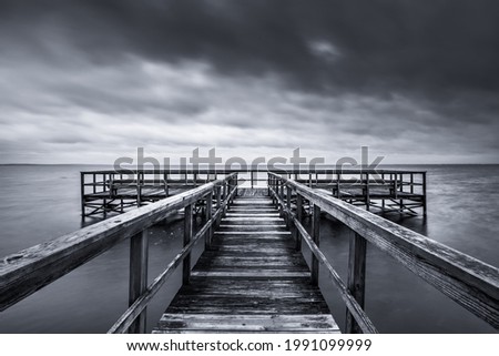 A dramatic grayscale of a weathered pier in the sea on background of the cloudy sky