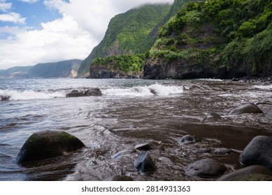 Dramatic green cliffs plunging to a black volcanic beach and breaking Atlantic waves at Seixal on the north coast of Madeira, Portugal.