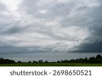 Dramatic grey storm clouds gathering over green rice field in countryside. Climate change impact weather patterns and powerful atmosphere of approaching storm in rural nature agricultural landscape.