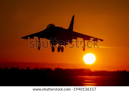 Dramatic Harrier jump jet comes into land at sunset with setting sun and orange sky background. AV-8 GR9 Matador named jet