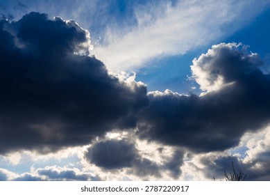Dramatic heavy storm clouds dominate the vast blue sky, while bright golden sun rays peek through the dark moody layers, creating a powerful contrast between light and shadow above
