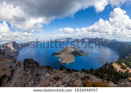 A dramatic high elevation view of the deep blue Crater Lake and Wizard Island from Watchman Tower on the Western rim with white fluffy clouds in late summer.