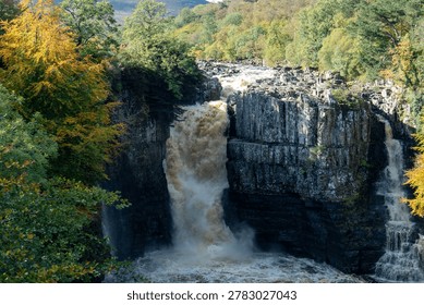 Dramatic High Force waterfall on the River Tees plunging between basalt cliffs amid autumn trees and mist. Middleton in Teesdale, County Durham, UK.