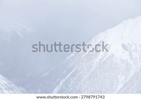 A dramatic high-altitude winter view featuring a snow-covered alpine mountain slope disappearing into dense whiteout conditions, mist, and heavy falling snow.